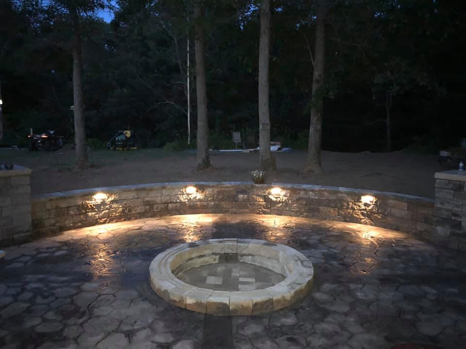 Outdoor fire pit with landscape lighting at night
